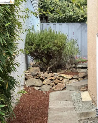 Tiered landscaping with natural rock retaining wall, mature shrubbery, and concrete stepping stones