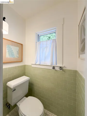 Green subway tile wainscoting, white hexagonal floor tiling, and a window with white trim