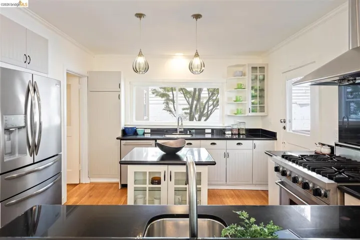 Kitchen featuring wood-finish flooring, white cabinetry, black countertops, and stainless steel appliances
