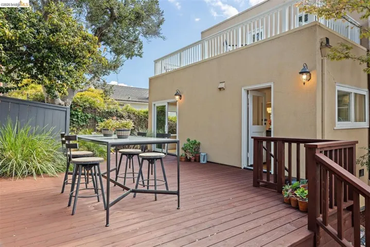Expansive wood-finish deck with exterior wall lighting, upper level balcony, and privacy fencing