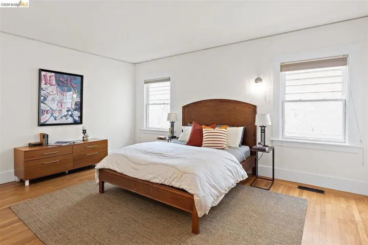 Hardwood flooring, two windows with trim, a wall-mounted light fixture, and a built-in ventilation grate