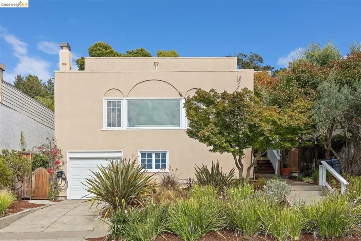 Stucco exterior with an arched window accent, attached garage, and established front landscaping