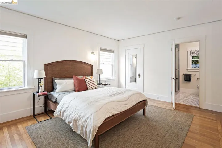 Hardwood flooring, painted trim, two windows, recessed wall lighting, and an attached bathroom with tiled flooring