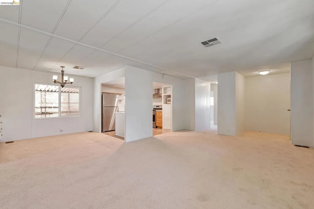 Unfurnished living room featuring light colored carpet and a chandelier
