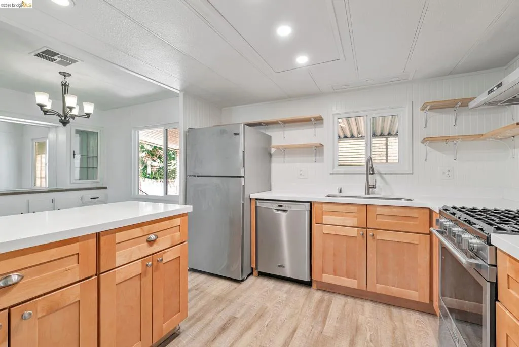Kitchen with open shelves, plenty of natural light, appliances with stainless steel finishes, light wood finished floors, and recessed lighting