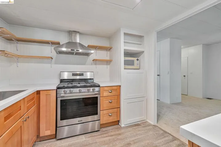 Kitchen with open shelves, stainless steel range with gas cooktop, island range hood, white microwave, and light wood-style floors