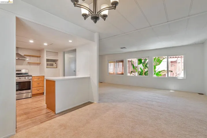 Kitchen featuring open shelves, gas stove, light countertops, light colored carpet, and open floor plan