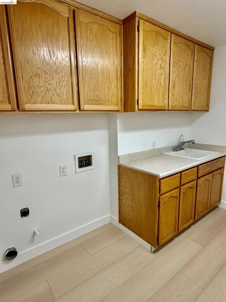 Wood-finish cabinetry, light-toned countertop, utility sink, and wood-finish flooring