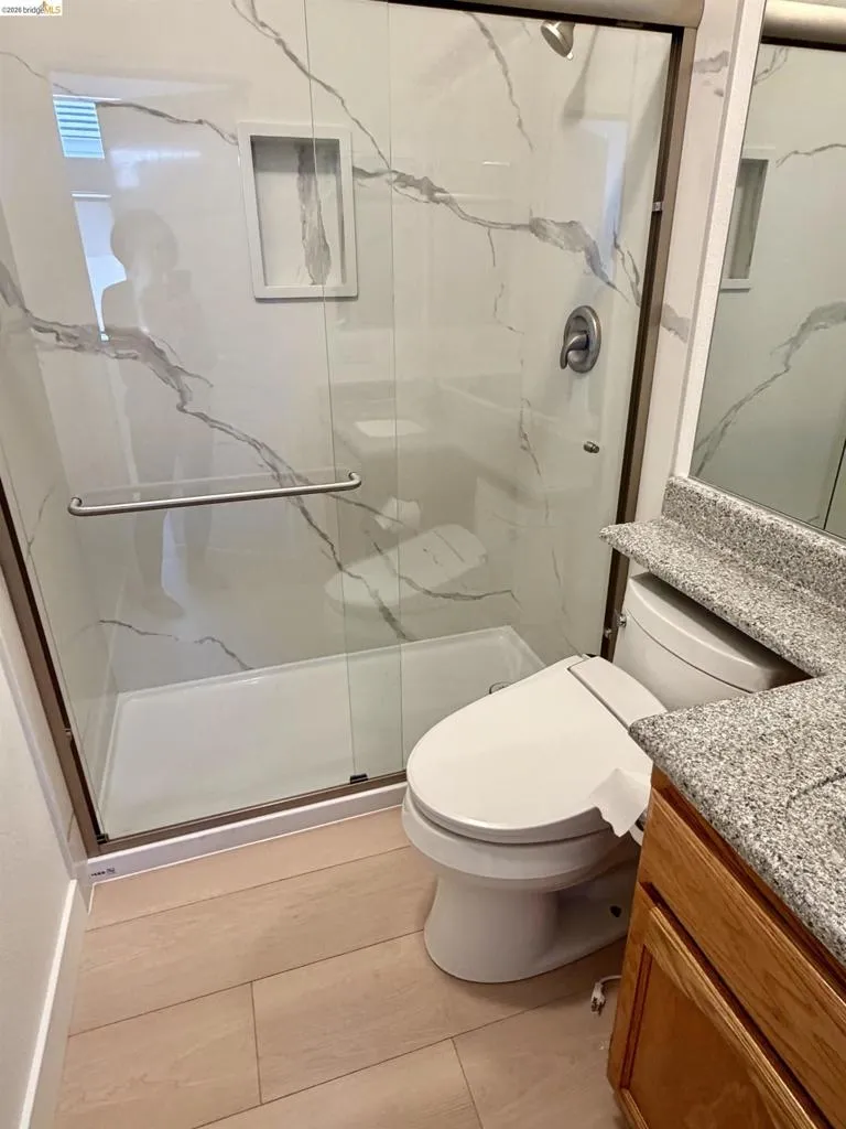 Glass-enclosed shower with white and grey-veined tile surround, integrated shower niche, and a contrasting shower pan