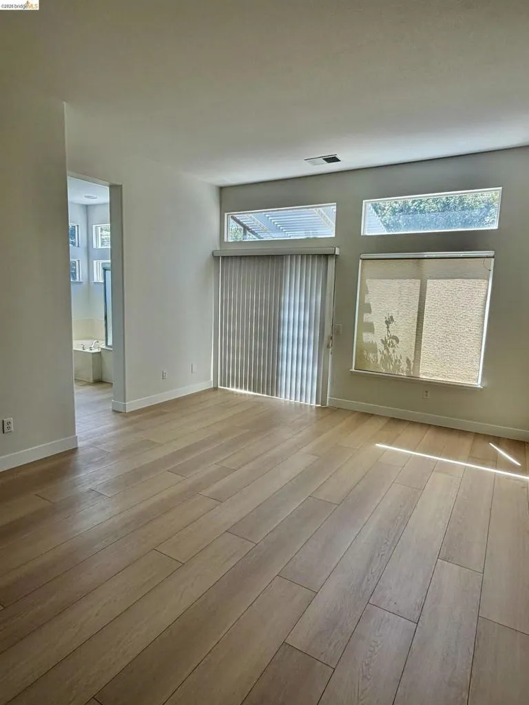Wood-finish flooring throughout, multiple transom windows, and a sliding glass door with vertical blinds