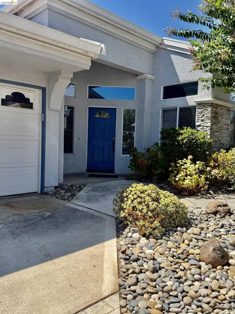Stucco exterior with stone accents, a deep blue entry door, an attached garage, and a rock-landscaped front yard
