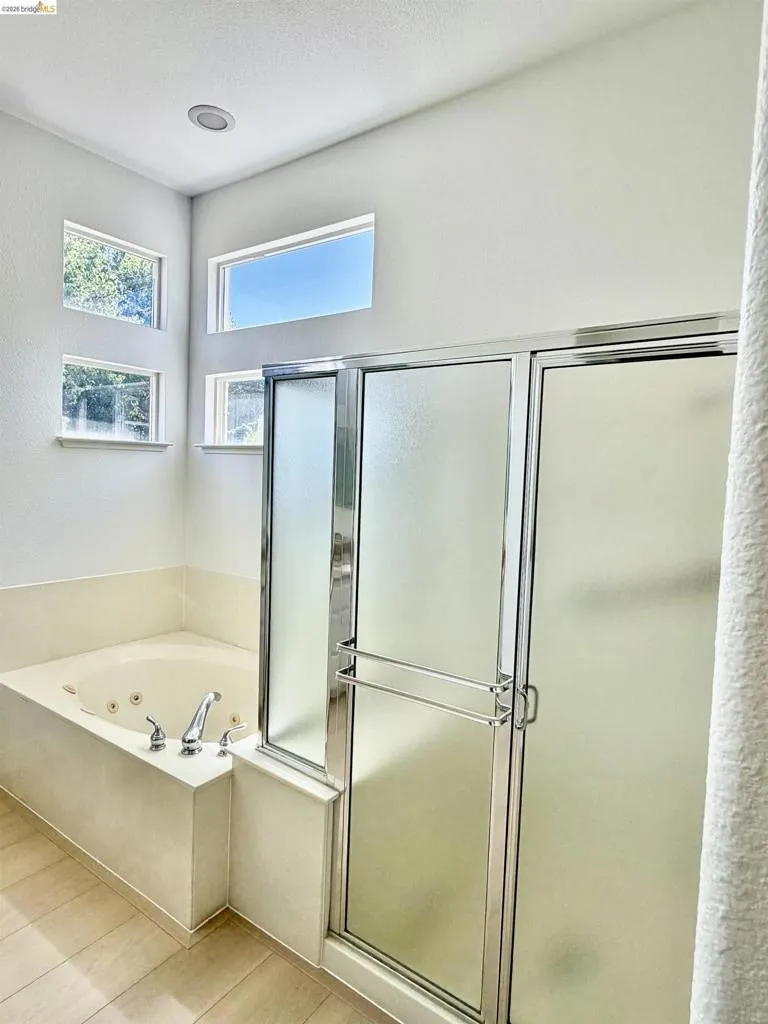 Soaking tub with chrome fixtures, tiled tub surround, and a glass-enclosed shower with frosted panels