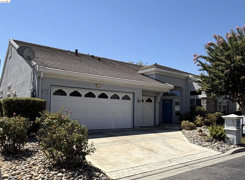 Stucco exterior with stone accents, a tile roof, an attached two-car garage, and a concrete driveway