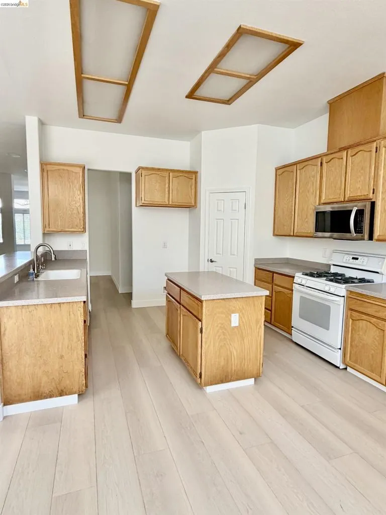 Kitchen featuring wood cabinetry, light-toned countertops, a center island, and wood-finish flooring