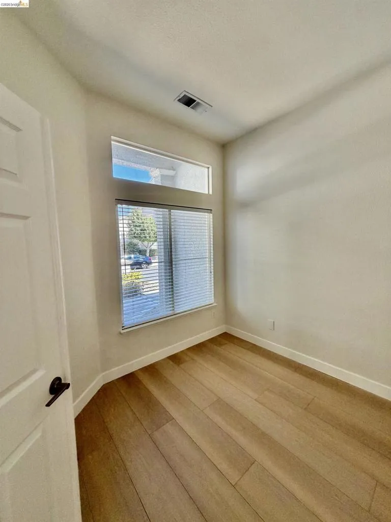 Wood-finish flooring with white baseboards, a window with blinds, and transom window