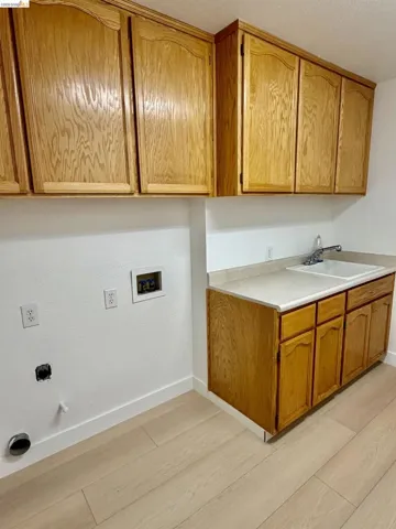 Wood-finish cabinetry, light-toned countertop, utility sink, and wood-finish flooring