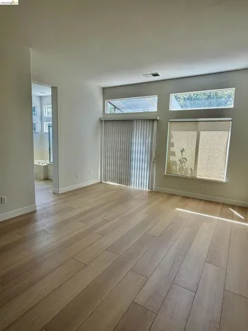 Wood-finish flooring throughout, multiple transom windows, and a sliding glass door with vertical blinds