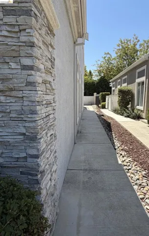 Stucco exterior with stone veneer accents, concrete pathway, and landscaping with river rock and shrubs