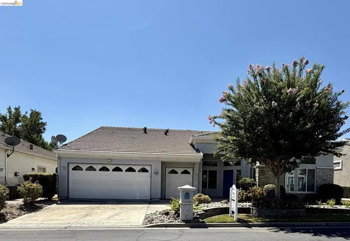 Single-story residence featuring a two-car garage, tile roof, and a low-maintenance front yard with mature landscaping