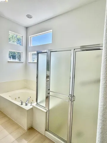 Soaking tub with chrome fixtures, tiled tub surround, and a glass-enclosed shower with frosted panels