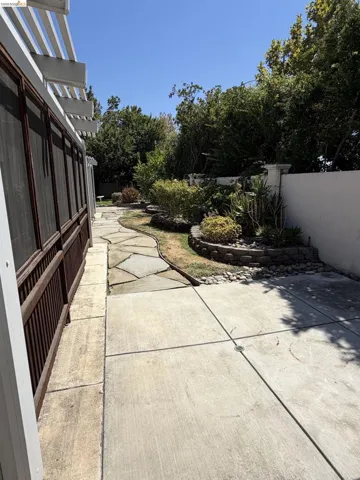 Concrete patio with an adjacent flagstone pathway, surrounded by mature landscaping and raised planters