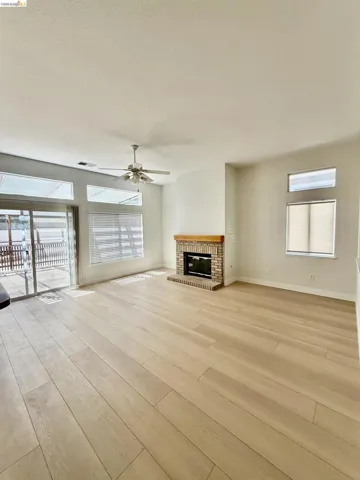 Spacious room featuring wood-finish flooring, a brick-surround fireplace with a wood mantle, and a ceiling fan