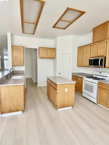 Kitchen featuring wood cabinetry, light-toned countertops, a center island, and wood-finish flooring