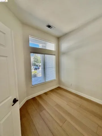 Wood-finish flooring with white baseboards, a window with blinds, and transom window