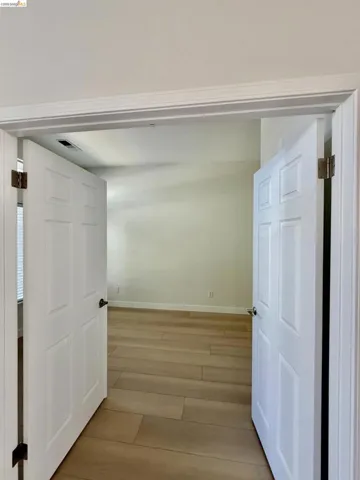 White paneled double doors open to a room with light wood-finish flooring