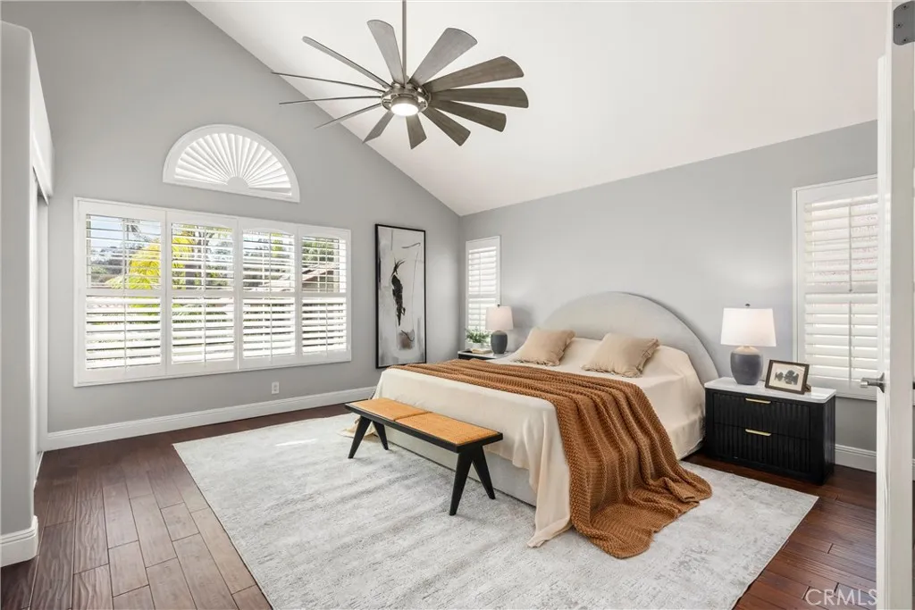 Serene primary suite with vaulted ceiling, plantation shutters, hardwood flooring and ceiling fan.