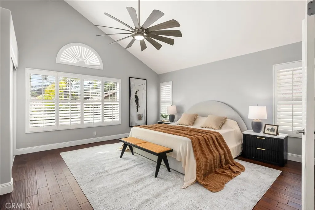 Serene primary suite with vaulted ceiling, plantation shutters, hardwood flooring and ceiling fan.