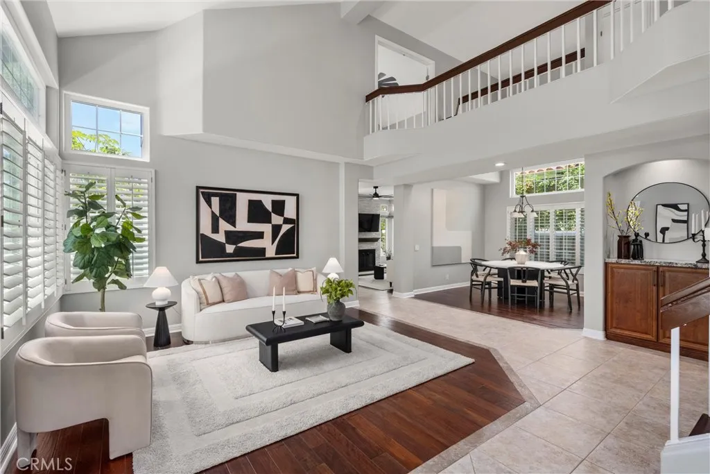 Light-filled living room with soaring ceilings, plantation shutters, hardwood floors, and an open-concept design.
