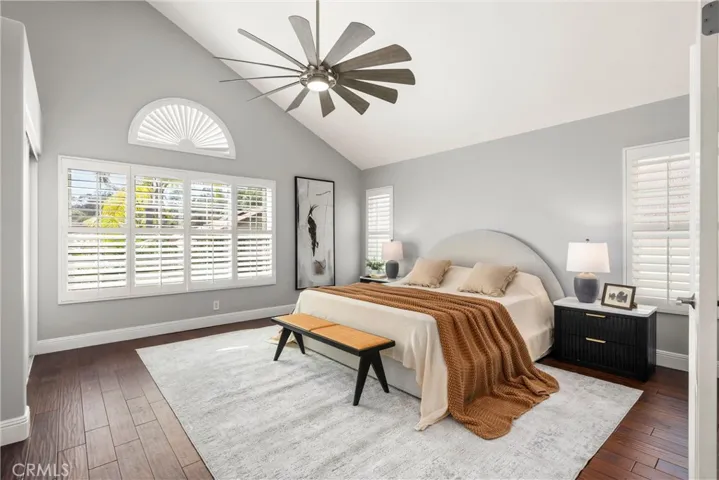 Serene primary suite with vaulted ceiling, plantation shutters, hardwood flooring and ceiling fan.