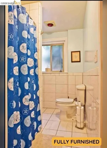 Recessed lighting, tiled shower surround, tiled flooring, toilet with standard flush, and a window with privacy glass