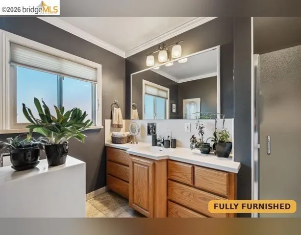 Shower stall alongside the wood-finished vanity with an integrated sink, broad mirror, and three-light vanity fixture.