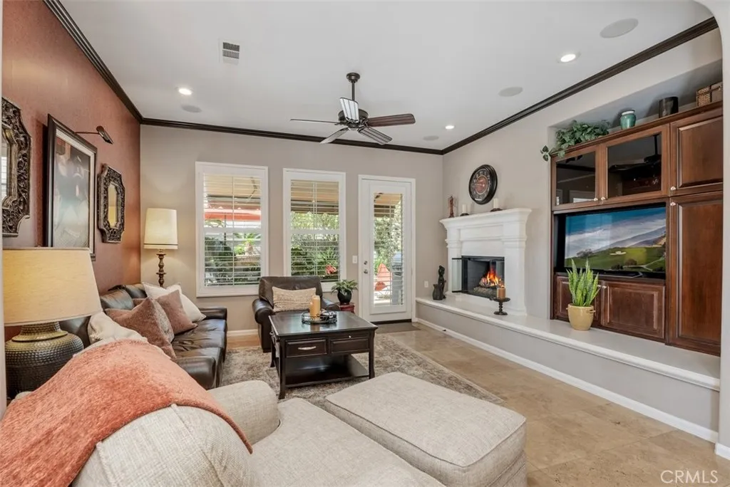 Set up for entertaining with built-in cabinet, surround sound, fireplace with molded mantle, ceiling fan, and door to a fantastic backyard