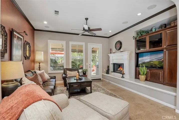 Set up for entertaining with built-in cabinet, surround sound, fireplace with molded mantle, ceiling fan, and door to a fantastic backyard