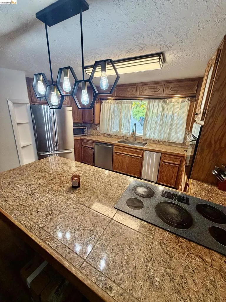 Kitchen featuring wood cabinetry, stainless steel appliances, a built-in cooktop, and a peninsula with a tile countertop