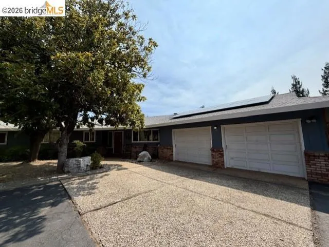 Single-story residence featuring a two-car garage with panel doors, brick accents, and solar panels on the roof
