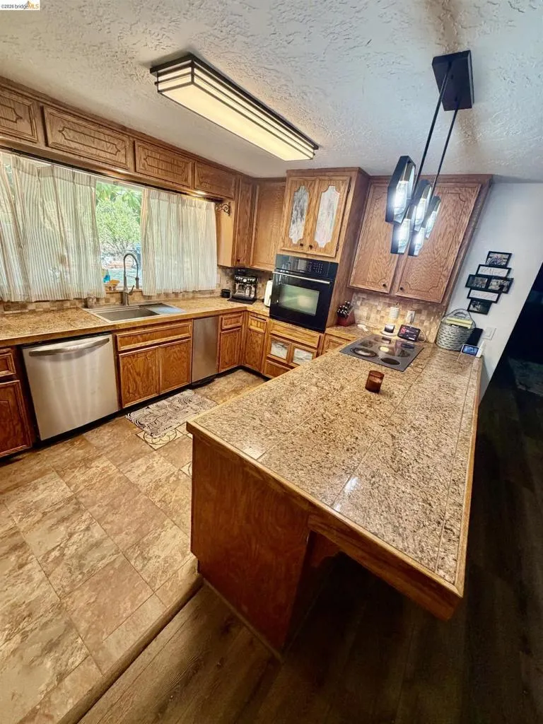 Wood cabinetry, built-in oven, stainless steel appliances, tiled countertops, and a multi-pendant light fixture
