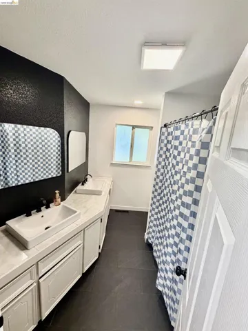 Dual vessel sinks with matte black fixtures, an extended vanity with white cabinetry, a frosted window, and dark floor tiling