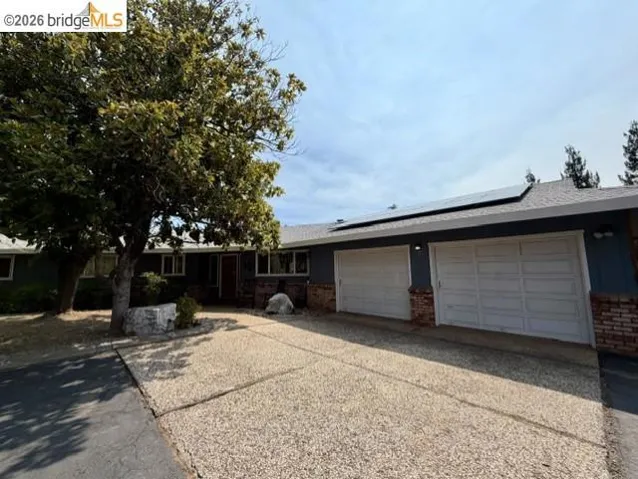Single-story residence featuring a two-car garage with panel doors, brick accents, and solar panels on the roof