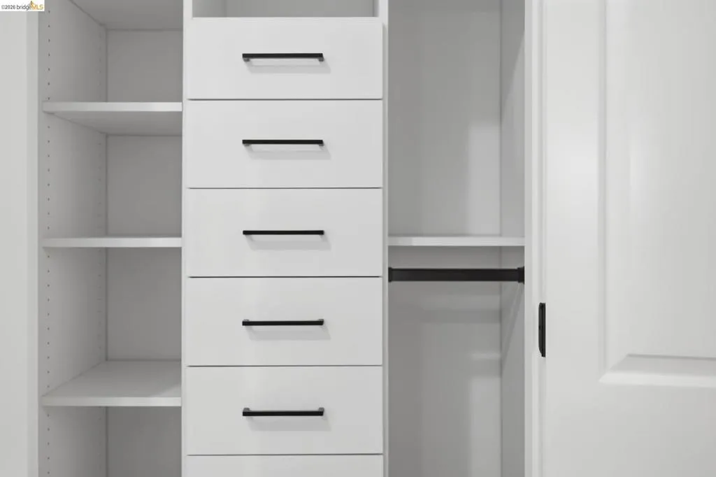 Built-in white cabinetry featuring multiple adjustable shelves, six drawers with matte black hardware, and an integrated hanging rod Built-in white cabinetry featuring multiple adjustable shelves, six drawers with matte black hardware, and an integrated hanging rod
