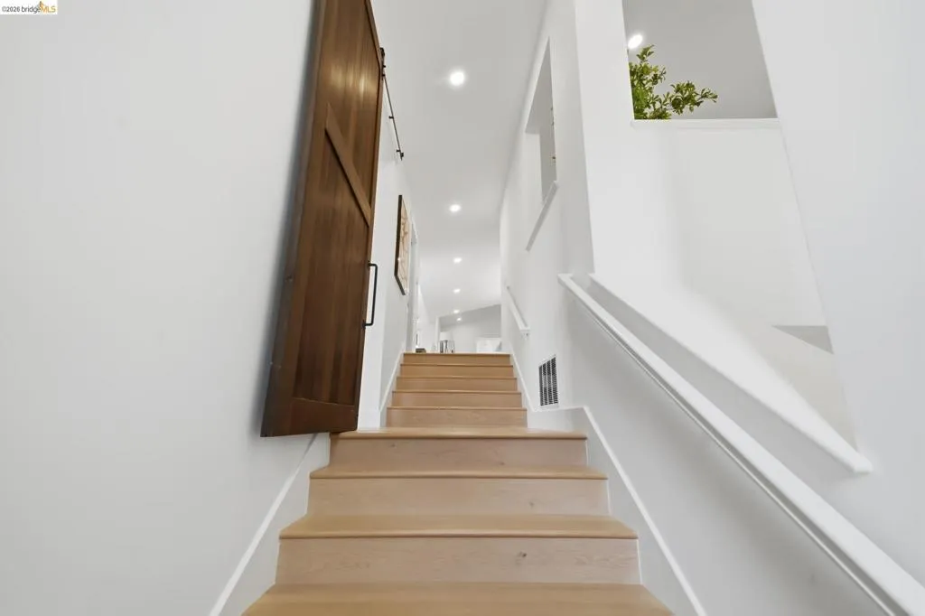 Wood-finish staircase with white risers, white wall-mounted handrail, and integrated ceiling lighting Wood-finish staircase with white risers, white wall-mounted handrail, and integrated ceiling lighting
