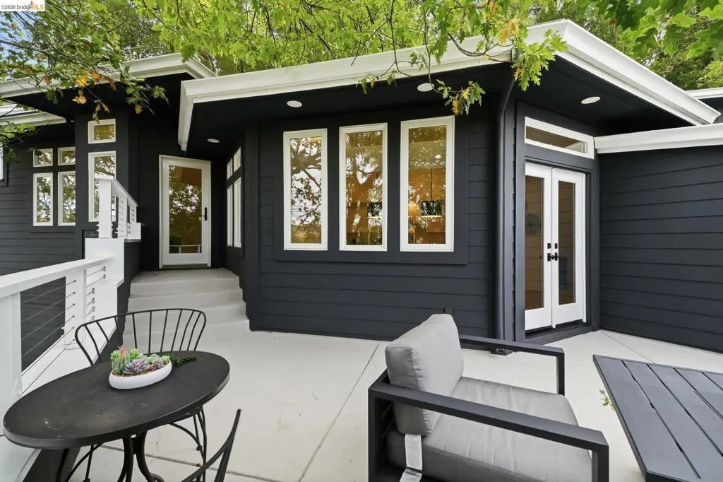 Exterior featuring dark siding, multiple large windows, a white cable railing, a concrete patio, and a white entry door Exterior featuring dark siding, multiple large windows, a white cable railing, a concrete patio, and a white entry door