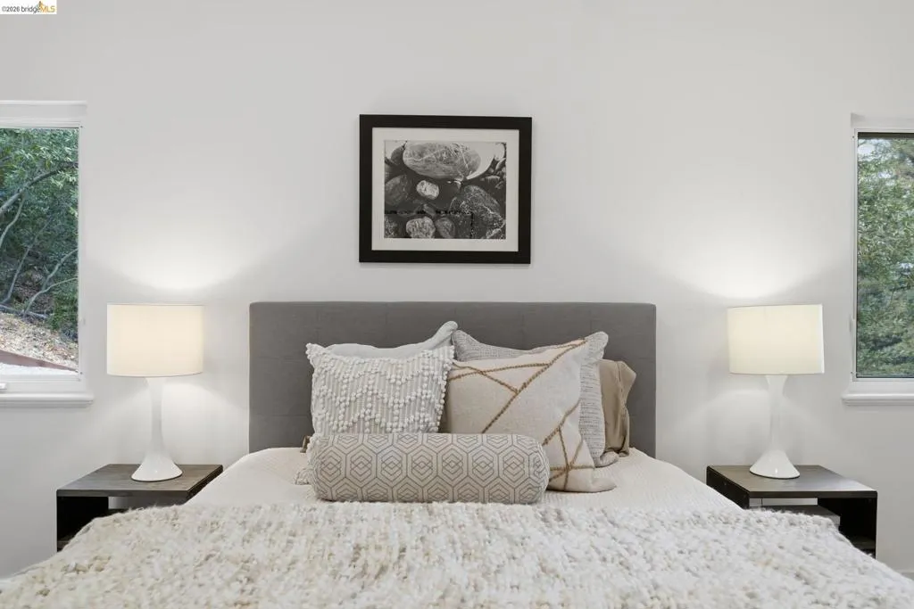 Built-in upholstered headboard, white walls, and dual side windows with natural scenery Built-in upholstered headboard, white walls, and dual side windows with natural scenery