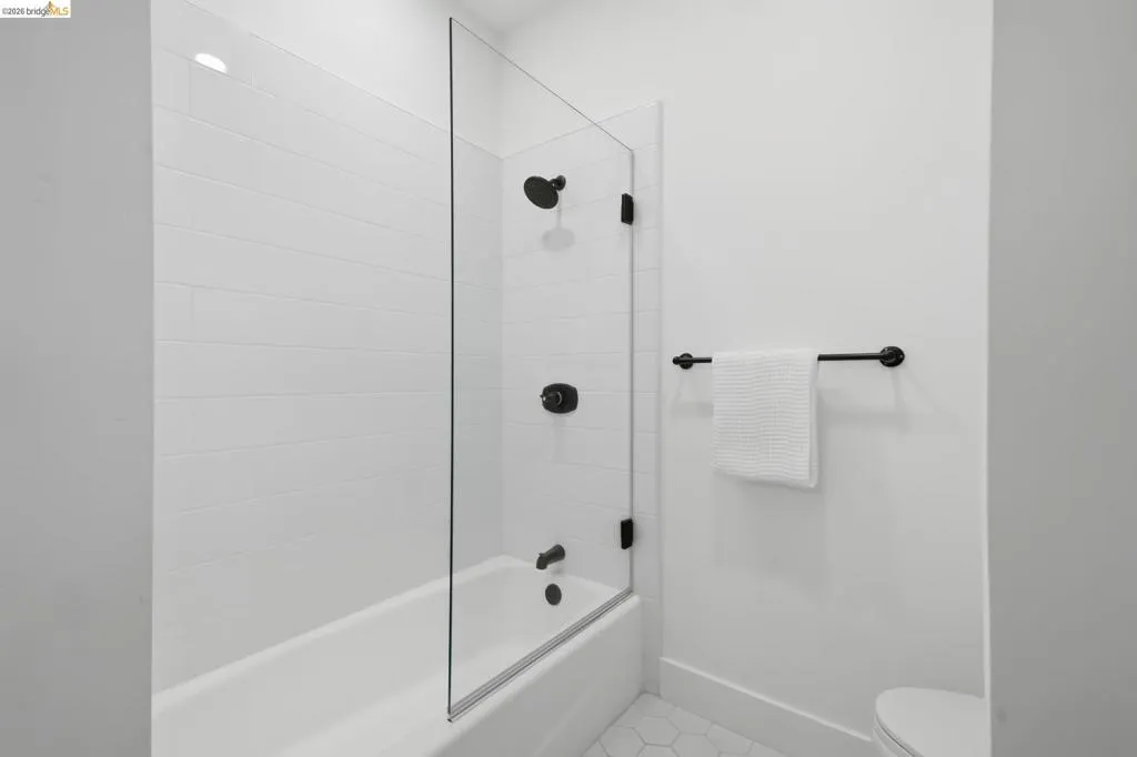 Bathtub with white subway tile surround, clear glass shower panel, matte black fixtures, and hexagonal floor tiles Bathtub with white subway tile surround, clear glass shower panel, matte black fixtures, and hexagonal floor tiles