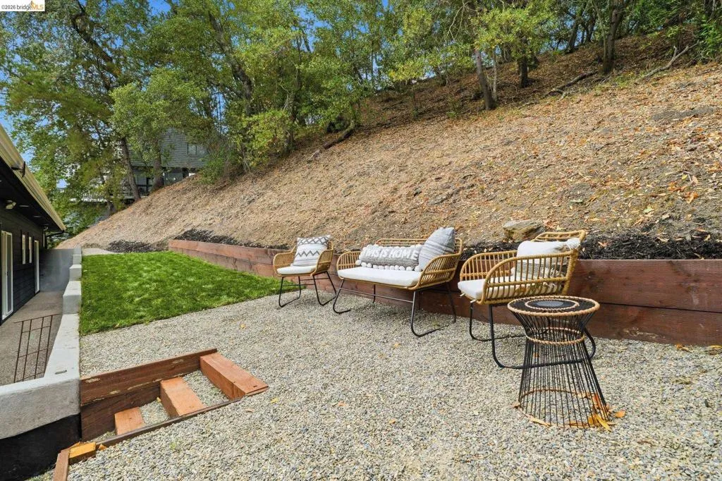 Gravel patio area with wood retaining walls, a section of manicured lawn, and mature trees in the background Gravel patio area with wood retaining walls, a section of manicured lawn, and mature trees in the background