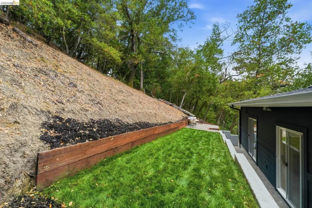 Manicured lawn area with a retaining wall, mature trees, and a concrete patio Manicured lawn area with a retaining wall, mature trees, and a concrete patio