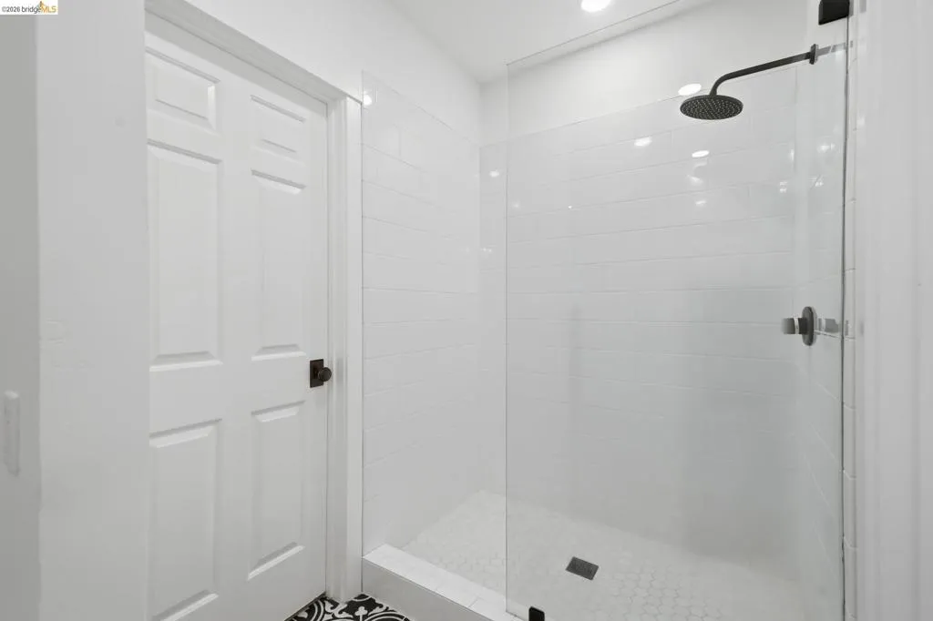 Enclosed shower with a glass panel, subway tile surround, hexagon tile flooring, and a matte black rain shower head Enclosed shower with a glass panel, subway tile surround, hexagon tile flooring, and a matte black rain shower head